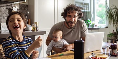 Man holding baby looking at computer while other son laughs