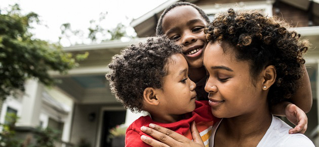 Mother holding two young sons in front of a house