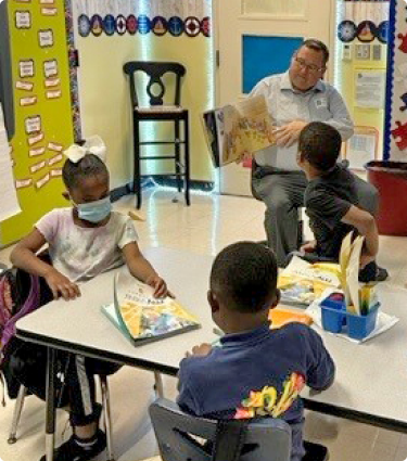 A volunteer from Protective reading to a group of young students in a classroom.