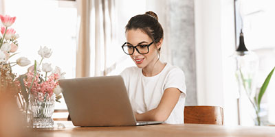 Young woman in glasses smiling, researching something on her computer. 