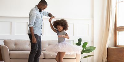 Father and daughter dancing at home, thankful that the father bought child life insurance. 