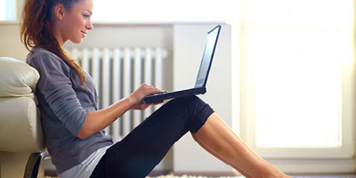 Woman sitting on the floor of her living room, smiling, looking at her computer.
