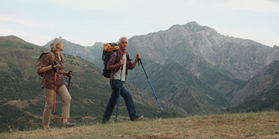  Older man hiking in the mountains with walking sticks and a backpack.