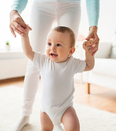 Smiling baby walking with help from mom