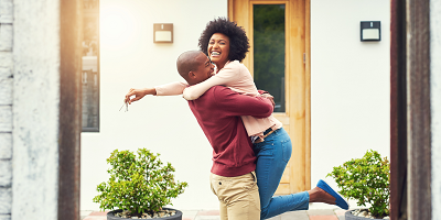 A woman riding on her husband's back in front of their new house