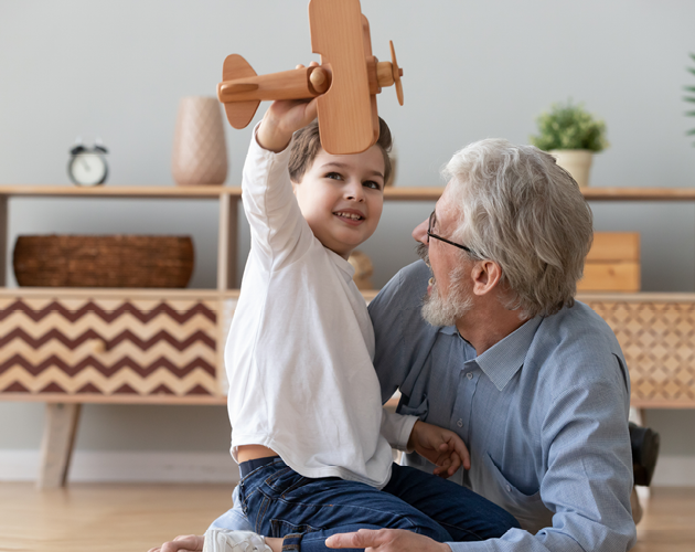A grandfather plays with his grandson who is holding a wooden airplane toy