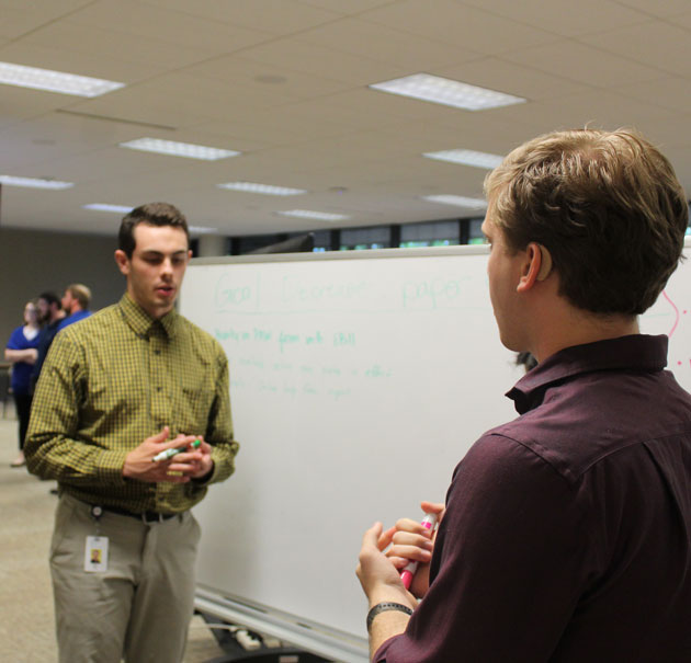 Three interns discuss a group project in front of a whiteboard