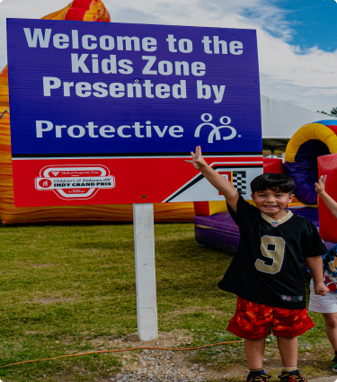 A smiling child poses in front of the Kids Zone area, sponsored by Protective, at the IndyCar for Children's of Alabama.