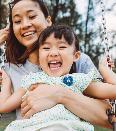 Laughing mom and daughter on a swing outdoors