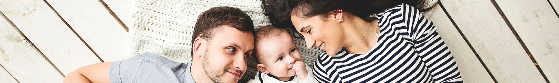 Husband and wife lay on the floor and smile at the baby between them