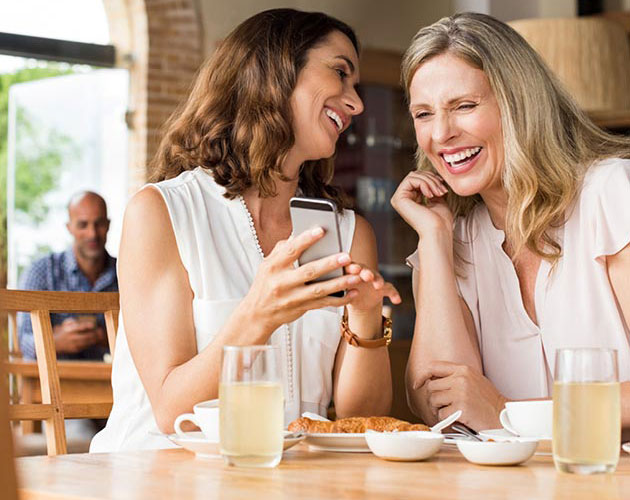 Two middle age women laugh while looking at a phone together