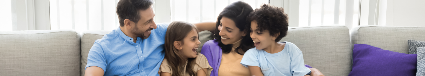 A man and woman laugh with their two children on a couch.