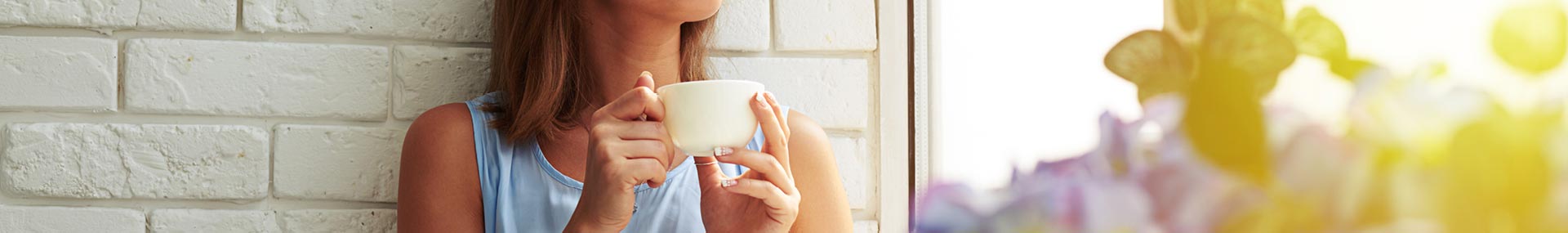 Woman holds a coffee cup while looking out the window at sunrise