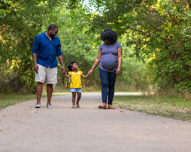 Pregnant woman walking down a trail with husband and young daughter