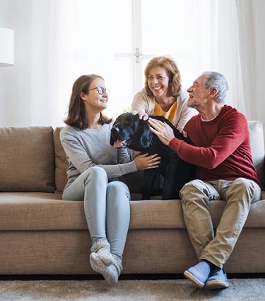 Grandparents sitting on couch with granddaughter and dog