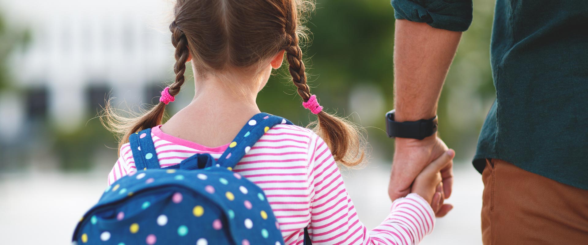 Young girl wearing backpack holding her father’s hand