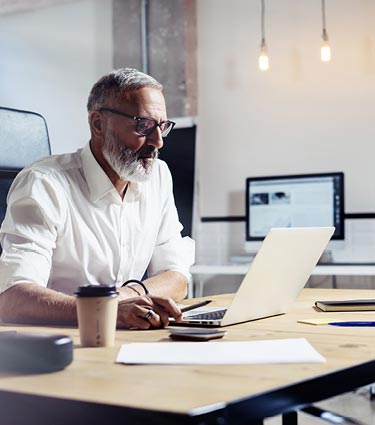 Middle-aged man with beard sitting at a desk with a laptop