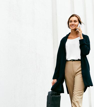 Young professional woman walking down city sidewalk with briefcase and smartphone