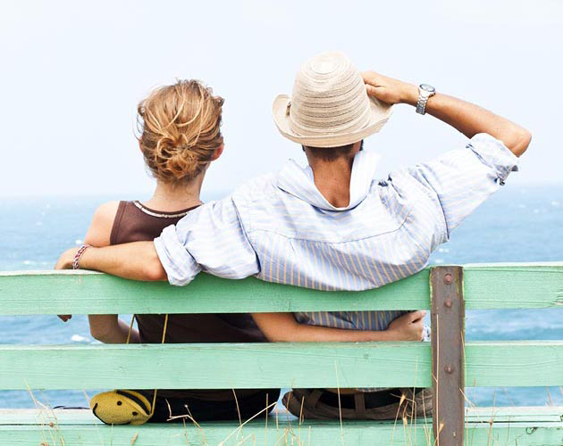 Man and woman sitting on bench overlooking ocean