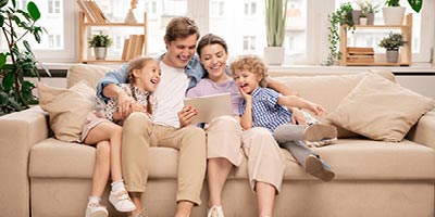 Young family with mom, dad and two kids sitting out the couch reading and laughing together.