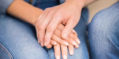 Close-up of a man’s hand on a woman’s hand, as if to offer comfort.