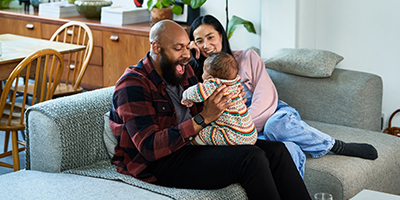 Man and woman sitting on couch laughing with their baby.