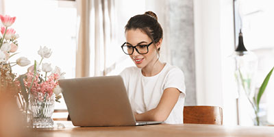 Young woman in glasses smiling, researching something on her computer.
