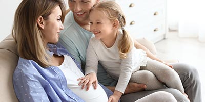 Pregnant mom sits with husband and young daughter