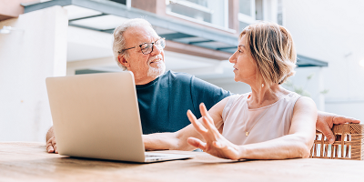 Senior couple sitting outside at table with laptop