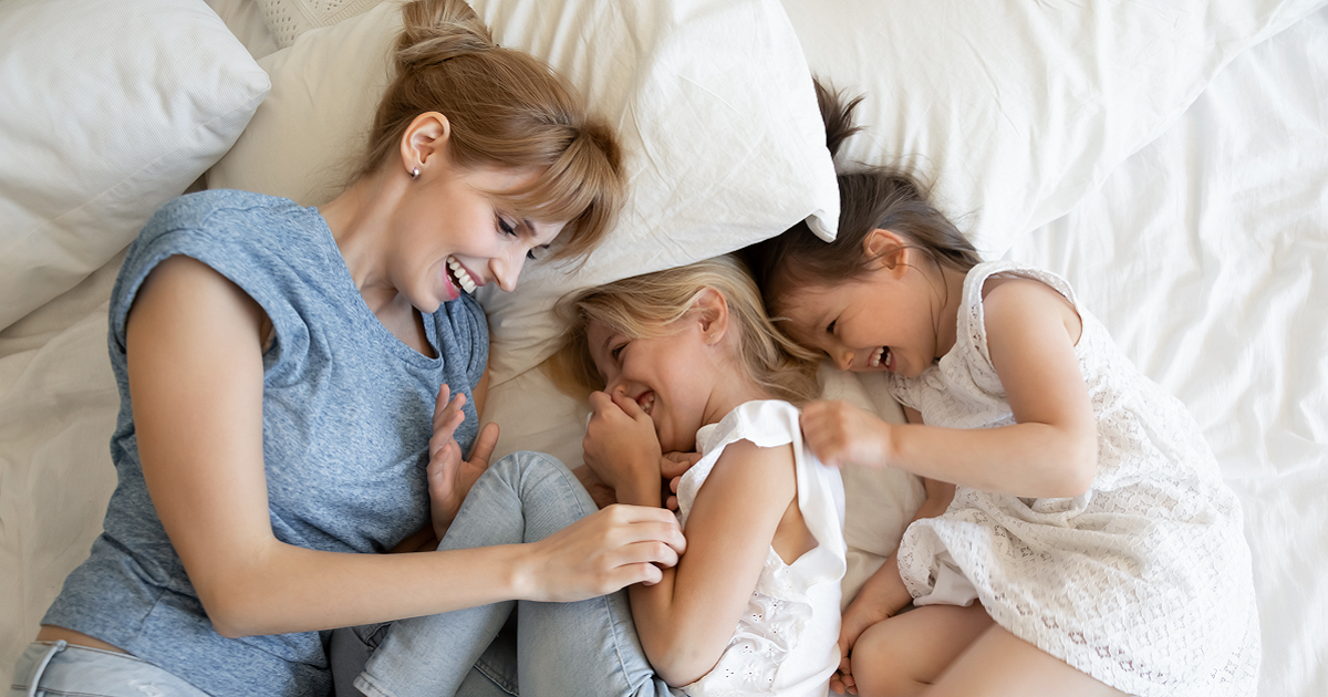 Woman and two young daughters lying in bed and laughing