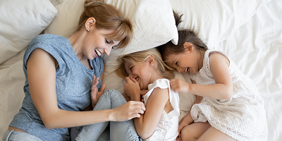 Woman and two young daughters lying in bed and laughing