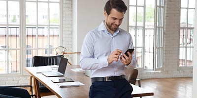 Young man at work and browsing his smartphone trying to understand what will happen with his life insurance exam.