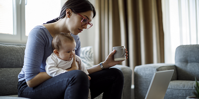 Mom on couch holding baby and looking at laptop