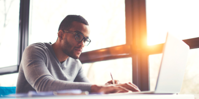 African American man writing something down as he researches an important topic on the internet.