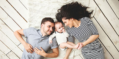 A family laying with their newborn considering types of life insurance for children they may purchase.