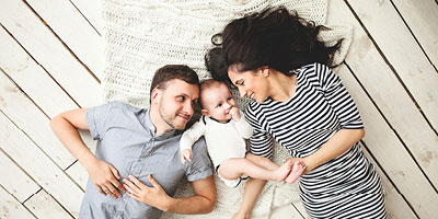 A family laying with their newborn considering types of life insurance for children they may purchase. 