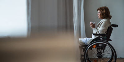 Woman sitting in a wheelchair looking out the window while drinking coffee.
