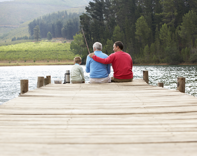 Father, adult son and young grandson fishing from pier on a lake.