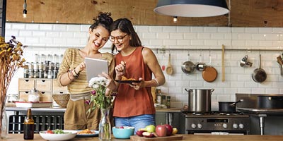 Two females looking and smiling while looking at their tablet computer and eating.