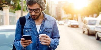 Young man walking, drinking coffee, and exploring credit insurance options on his smartphone. 