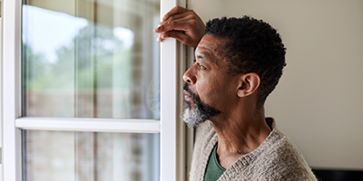 African-American man gazes out the window of his home.