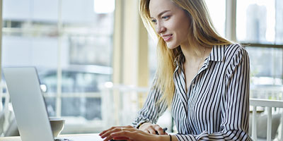Young woman sitting at a desk and browsing the internet on a laptop.