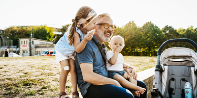 Man sits outdoors on a sunny day with two young children.