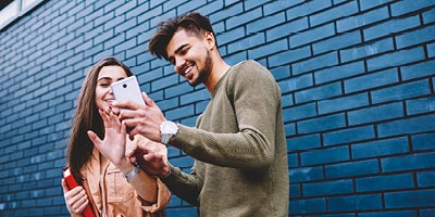 A man smiling and showing his female friend his phone.