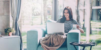 Female starting her morning with a cup of coffee and reading about life insurance on her computer.