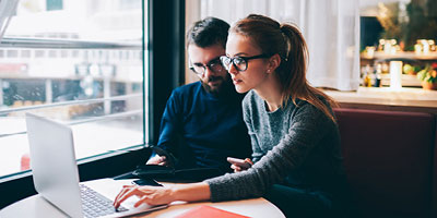 Couple at coffee shop paying bills on laptop