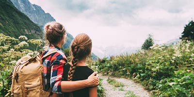 Mom with arm around teenage daughter as they look at a mountain in the distance from hiking trail