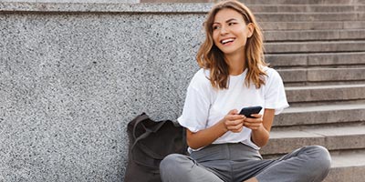 Millennial woman browsing her smartphone on the steps of a building.