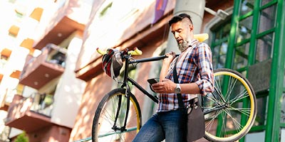 Man looking at his phone while holding his bike in a downtown area.