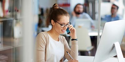 Young woman professionally dressed taking notes while on the phone.